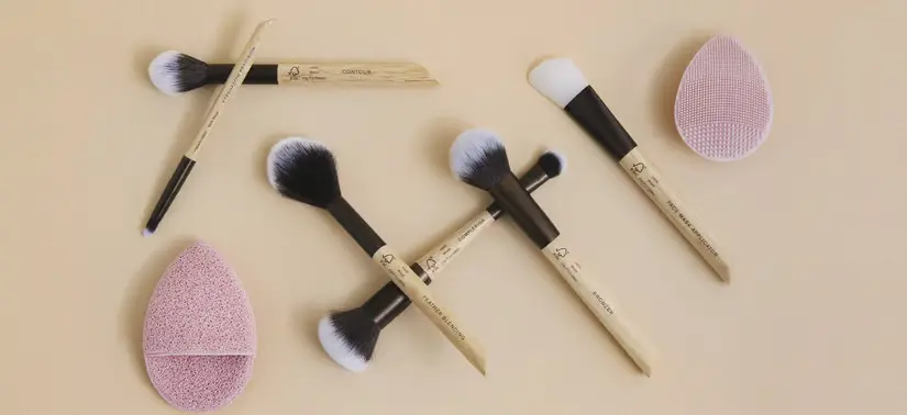 Her ses en beige baggrund med flere forskellige M.Cosmetics produkter liggende.