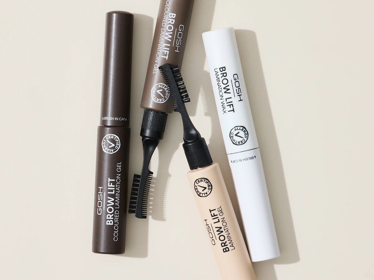 Her ses forskellige Brow Lift-produkter fra GOSH Copenhagen arrangeret mod en lys baggrund. Produkterne omfatter Coloured Lamination Gel og Lamination Wax i forskellige nuancer samt tilhørende brynbørster.