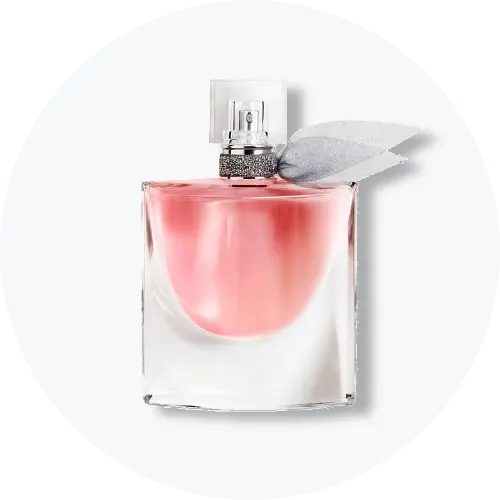Her ses en transparent parfumeflakon med rosa indhold, sølvfarvet spraytop og et dekorativt gråt bånd ved flakonens hals. Produktet står centralt mod en lys, rund baggrund.