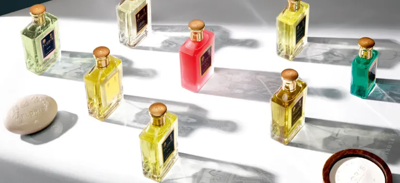 Flere Floris London parfumeflasker i forskellige farver står spredt i sollys på en hvid flade, omgivet af sæbe og dekorative detaljer.
