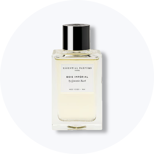 Her ses et billede af en parfumeflakon fra Essential Parfums placeret centralt mod en lys, rund baggrund. På flakonen står teksten “ESSENTIAL PARFUMS PARIS BOIS IMPÉRIAL by Quentin Bisch”. Flakonen er i klart glas med sort låg.