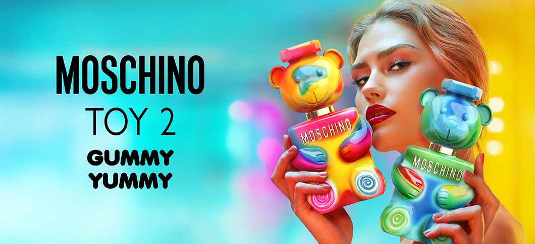 Her ses et billede med en person til højre, der holder to parfumeflakoner formet som bamser i farverige nuancer. Til venstre står teksten “MOSCHINO TOY 2 GUMMY YUMMY”.