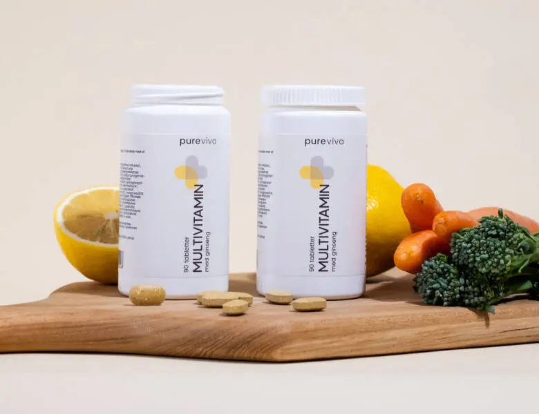 Her ses en grøn lys baggrund to stående vitamin plastik bøtter i hvis stående på et træskærebræt. Der ligger piller samt frugt og grønt ved siden af produkterne oven på brættet.