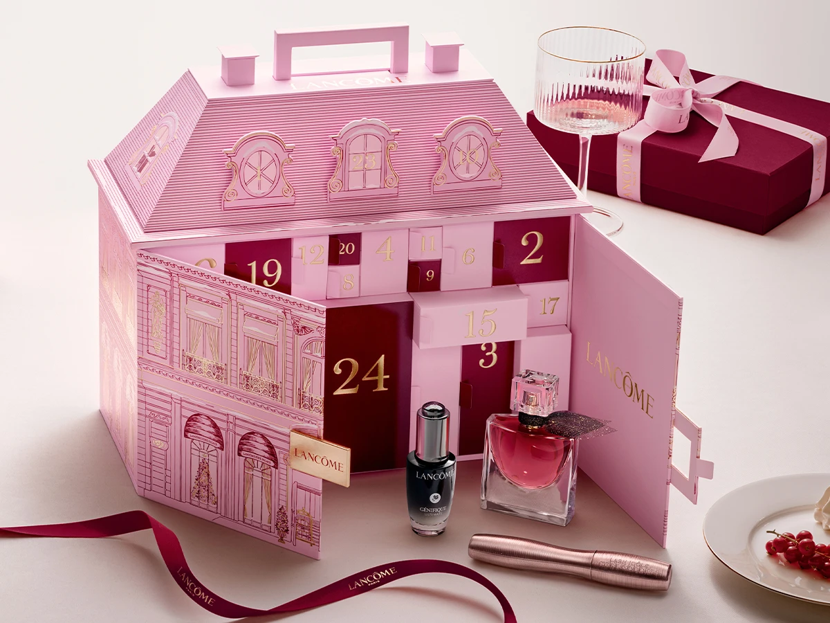 Lyserød Lancôme julekalender formet som et hus, med åbne låger der afslører Génifique serum, La Vie Est Belle parfume og mascara.