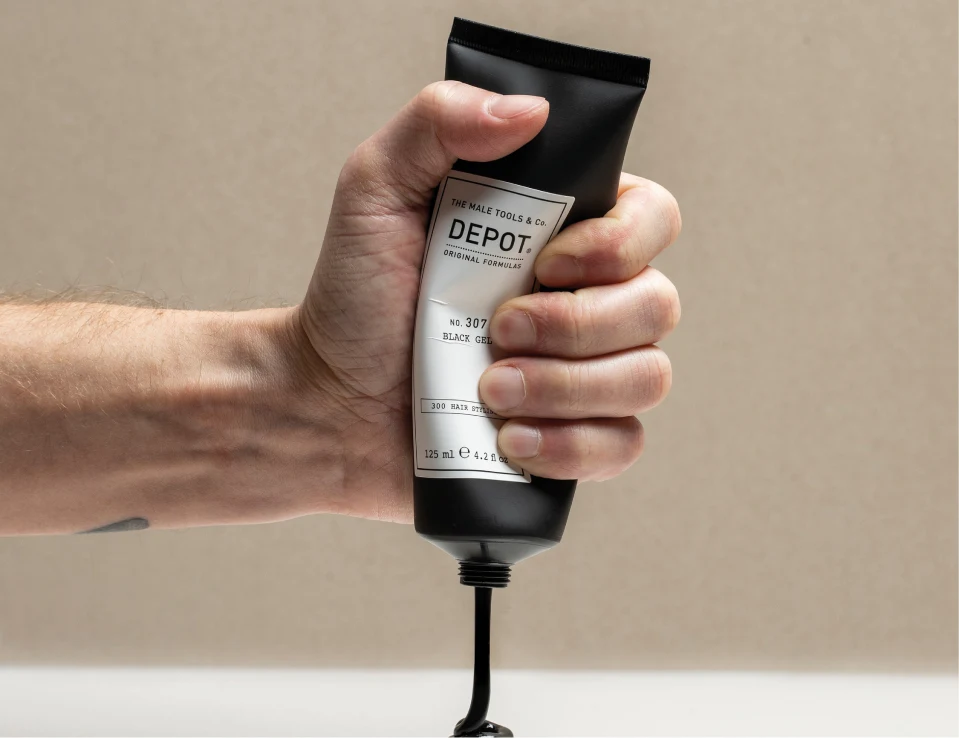 Her ses en hånd, der holder DEPOT No. 307 Black Gel i en sort tube. Sort gel løber ud fra tubens åbning.