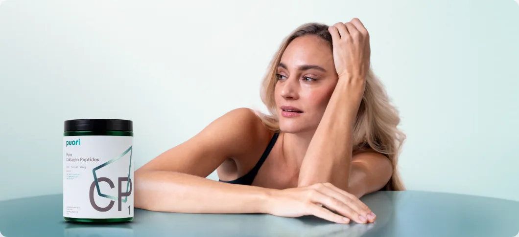 Kvinde læner sig mod et bord og ser til siden på lys blågrøn baggrund, mens en bøtte Puori Collagen Peptides står til venstre i billedet.