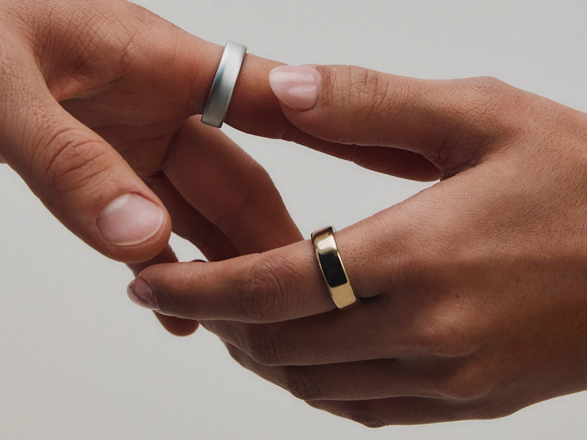 To hænder, den ene med en sølvfarvet ring og den anden med en guldfarvet ring, der forsigtigt rører hinanden.