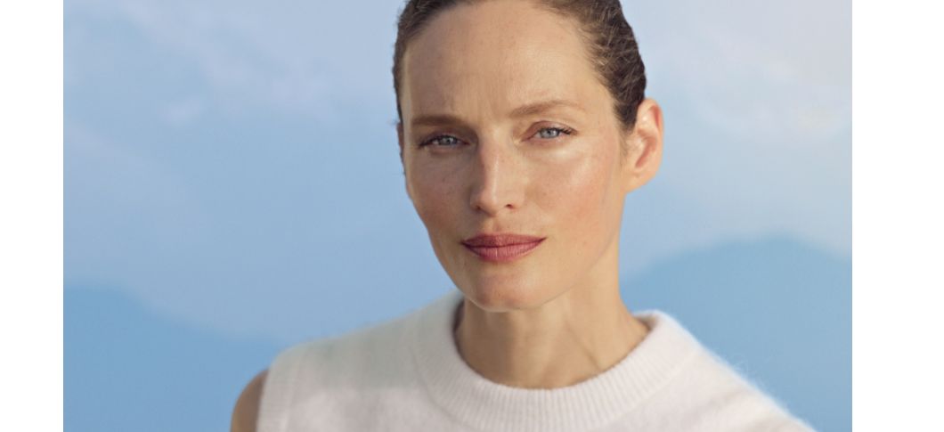 Banner fra WELEDA med en kvinde med naturlig glød i ansigtet og håret sat tilbage, iført en lys top foran en lyseblå baggrund.