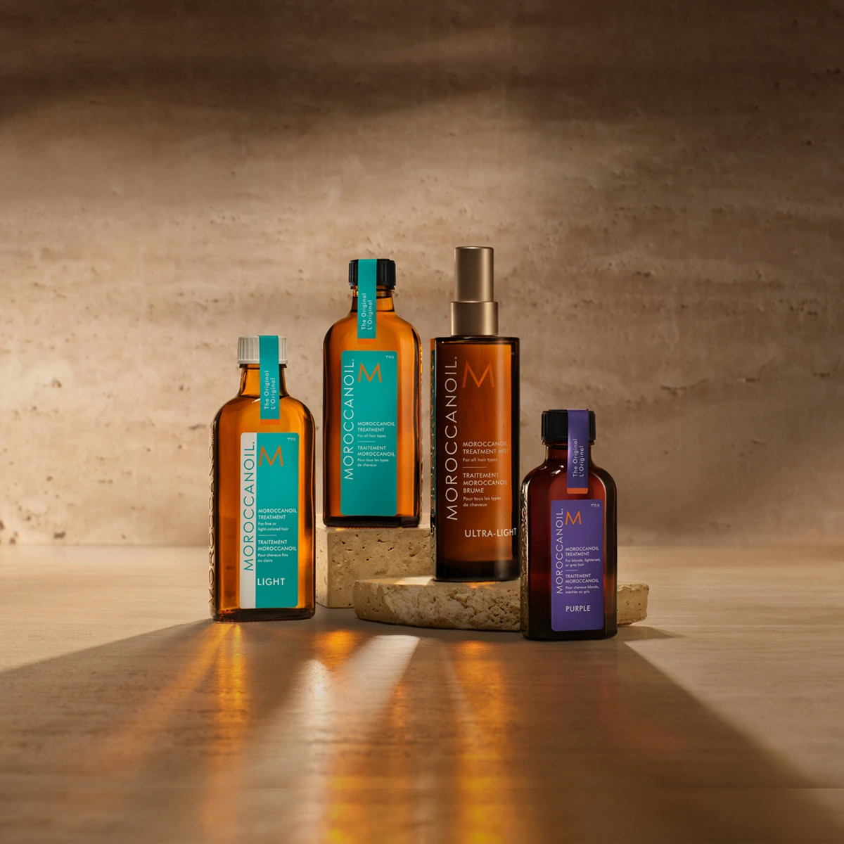 Fire Moroccanoil hårprodukter: Light, Treatment, Ultra-Light Treatment Mist og Purple Treatment, arrangeret på en tekstureret overflade.