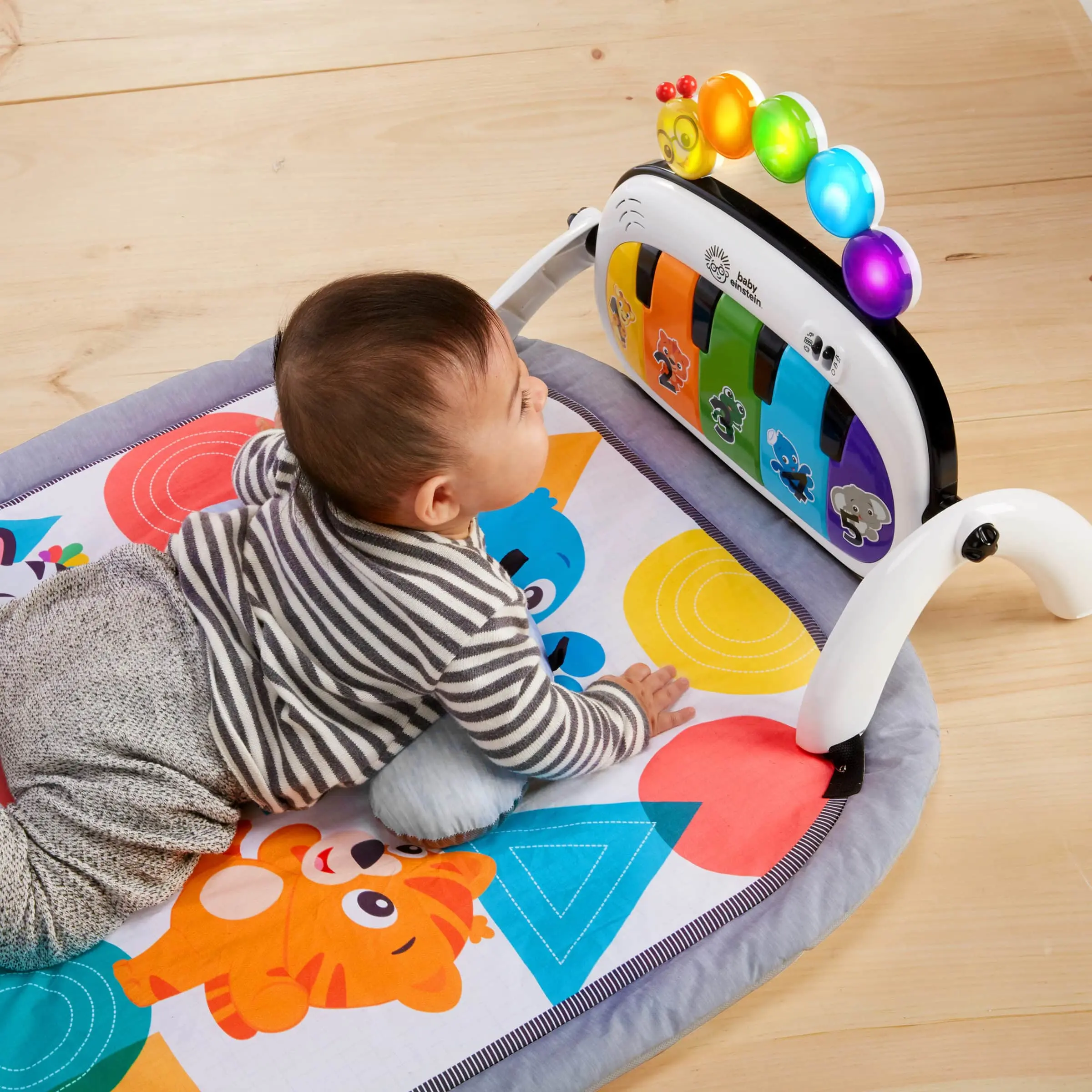 Baby ligger på maven på en farverig legemåtte og kigger på et interaktivt legetøjspiano med lys og dyremotiver.