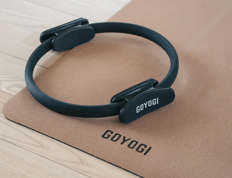 Sort pilatesring ligger på en korkmåtte med GOYOGI-logo på et lyst trægulv.
