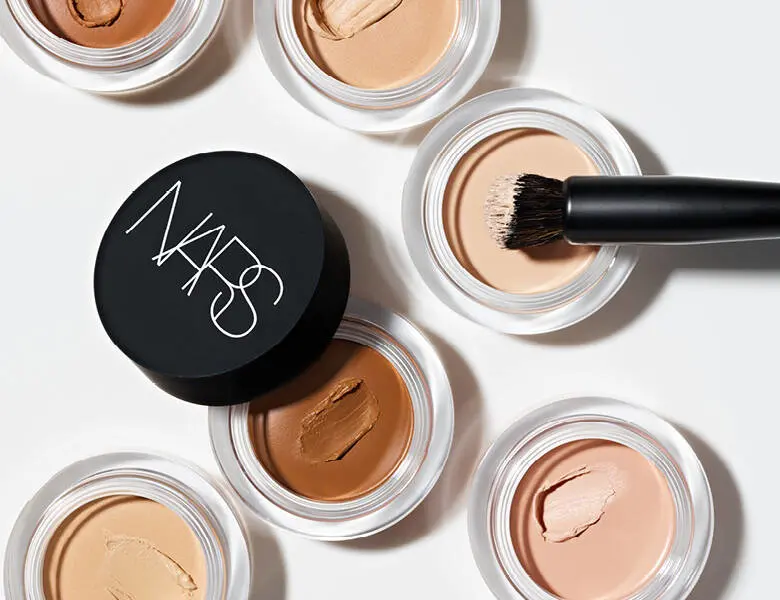 Her ses en hvid baggrund med flere åbne Nars concealers i forskellige farver. 