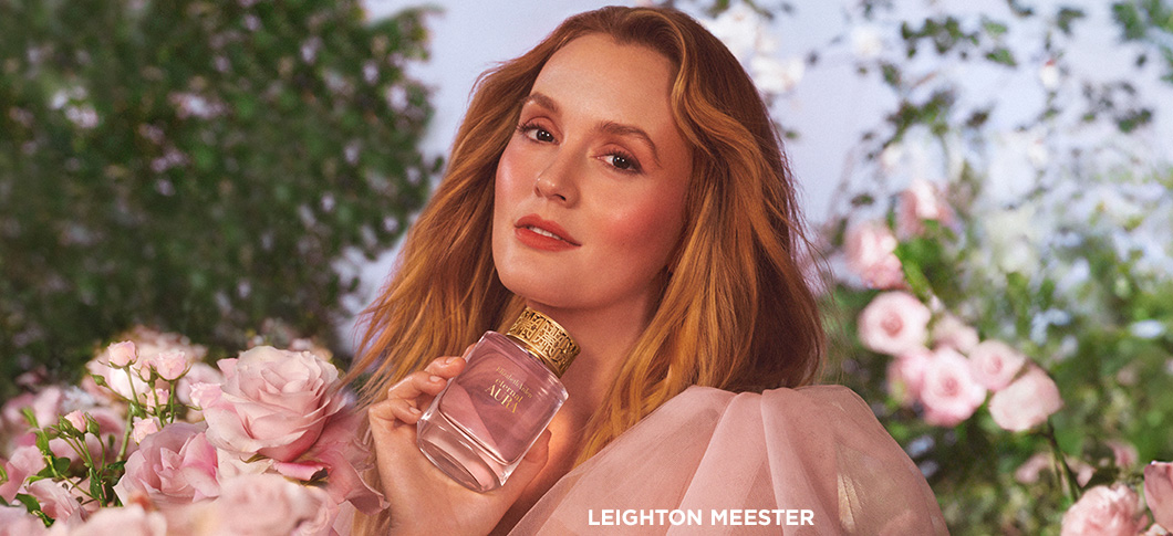 Her ses en kvinde, der holder en Elizabeth Arden parfume omgivet af lyserøde blomster i en have.