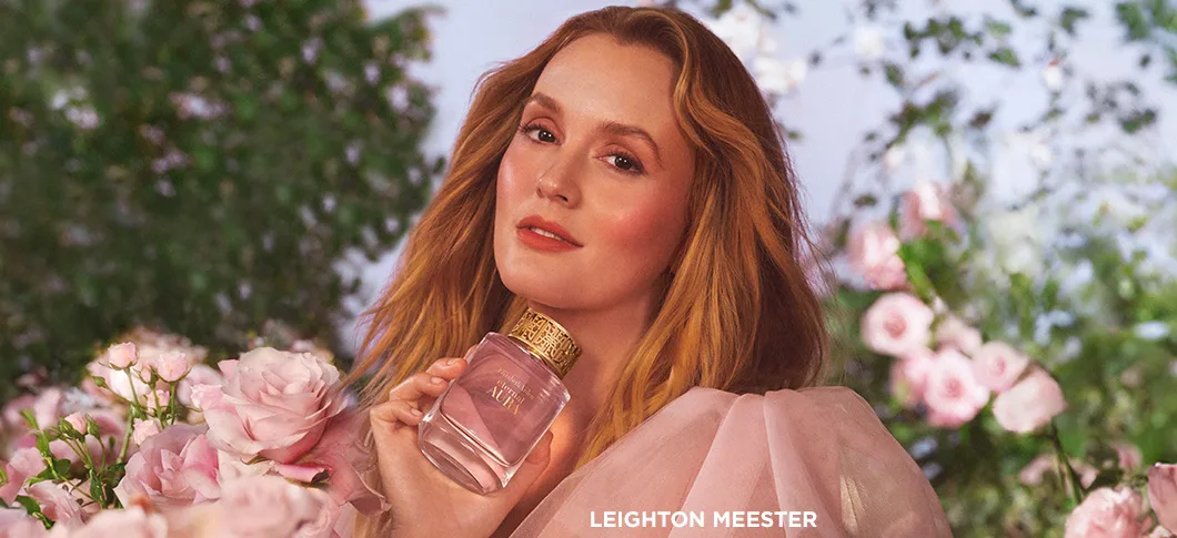 Her ses en kvinde, der holder en Elizabeth Arden parfume omgivet af lyserøde blomster i en have.