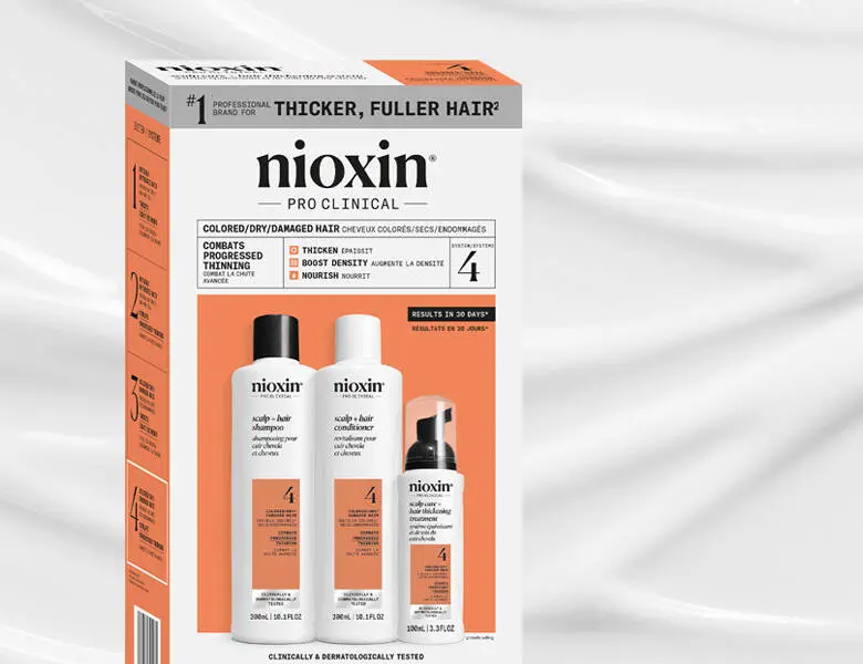 Her ses et billede af et hårplejekit fra Nioxin placeret mod en lys baggrund. På æsken står teksten “nioxin PRO CLINICAL” samt “THICKER, FULLER HAIR”. Sættet indeholder shampoo, conditioner og treatment-produkter.