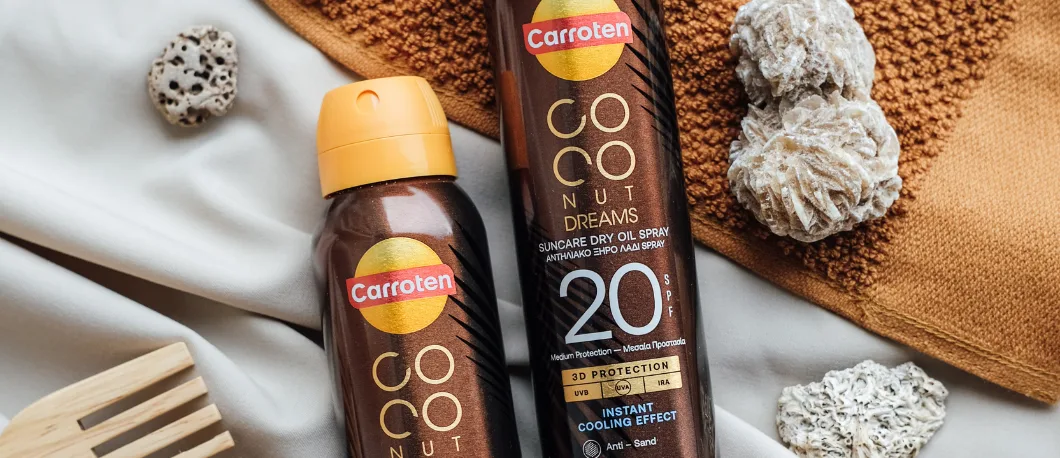 Her ses Carroten Coconut Dreams solspray med SPF 20 omgivet af strandinspirerede elementer som håndklæde, sten og trædetaljer.