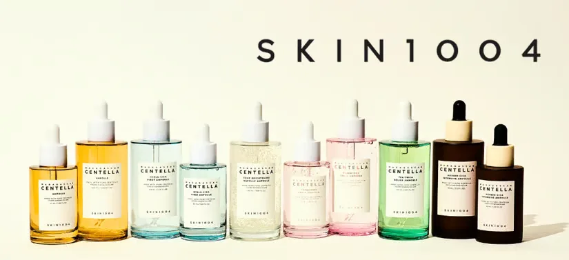 Her ses en lys baggrund med mange forskellige Skin1004 produkter i forskellige farver på en række. I højre øverste hjørne ses deres logo.