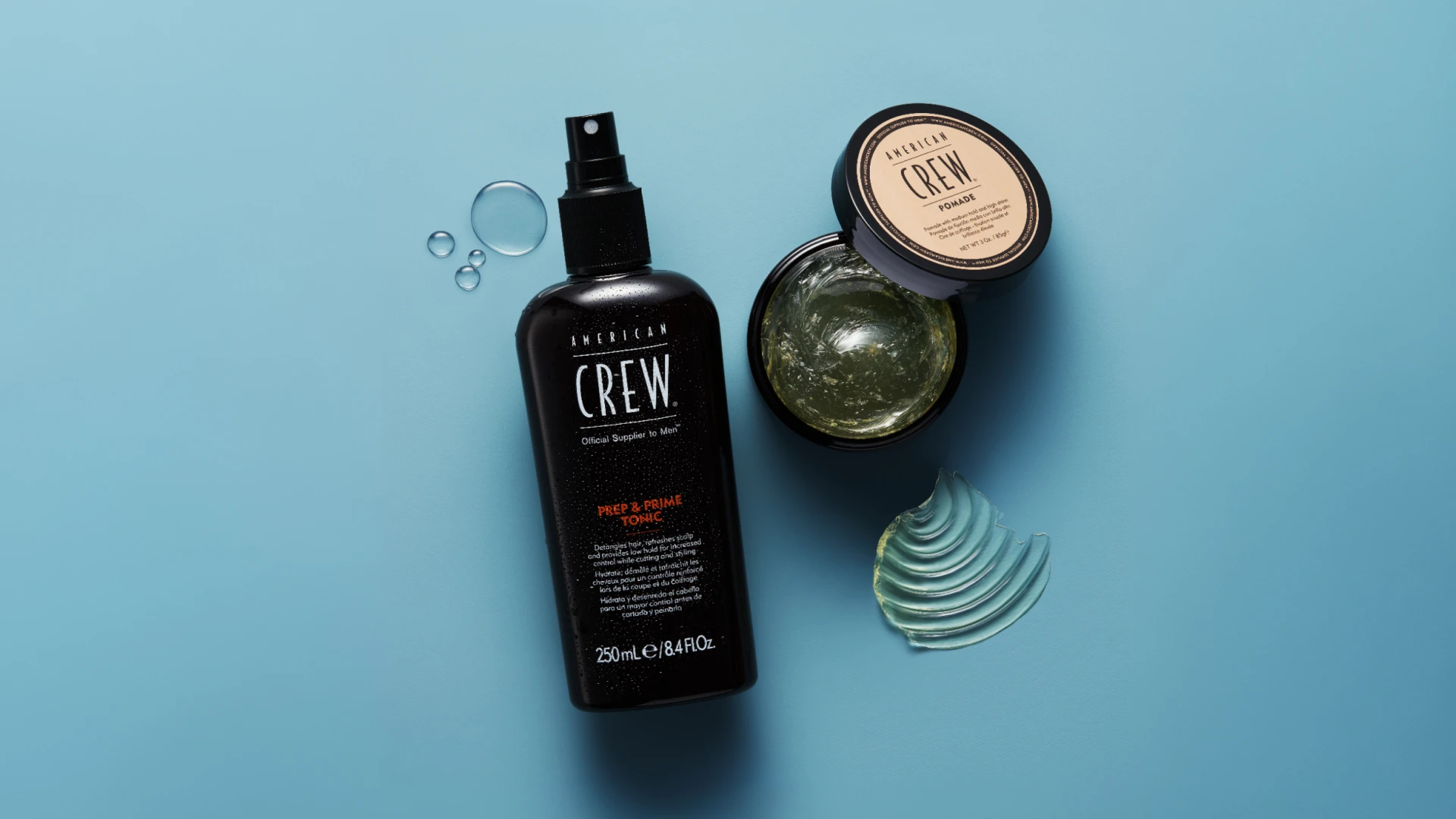 American Crew Prep & Prime Tonic sprayflaske og åben krukke med Pomade på blå baggrund med vanddråber.