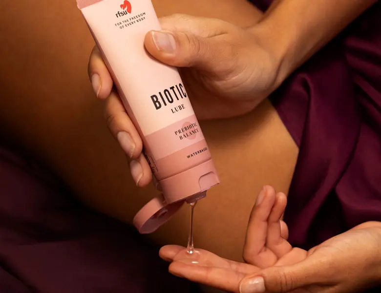 Person hælder RFSU Biotic Lube ud i hånden. Produktet er i lyserød emballage.