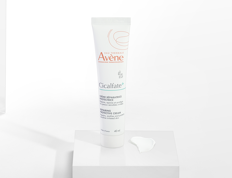 Her ses en Avène Cicalfate+ creme i hvid emballage på en lys baggrund med creme ved siden af.
