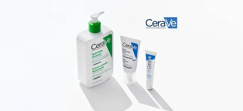 Tre hudplejeprodukter fra CeraVe står på en lys, ensfarvet baggrund med bløde skygger. Til venstre ses en stor, hvid pumpeflaske med grøn pumpe og grøn label med teksten “Hydrating Cleanser”. Til højre for den står to mindre, hvide tuber med blå detaljer og CeraVe-logoet. Produkterne er placeret med lidt afstand imellem, så hver enkelt fremstår tydeligt. Øverst til højre i billedet ses CeraVe-logoet. Udtrykket er rent, klinisk og enkelt med fokus på produkterne.