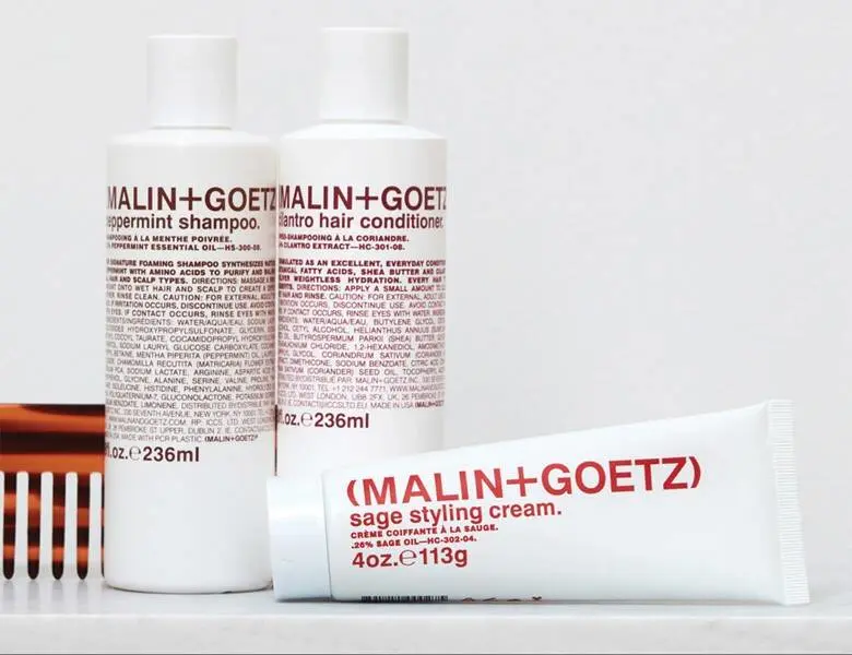 Her ses en hvid baggrund med tre hvide Malin+Goetz produkter, som alle har rød skrift.