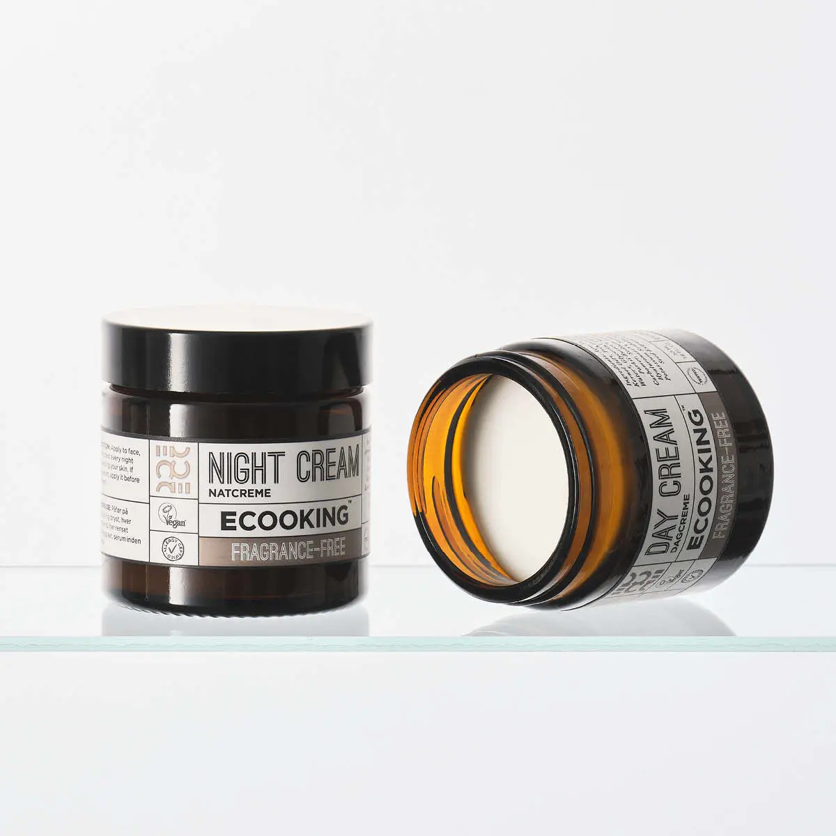 To Ecooking krukker med ansigtscreme. En stående Natcreme og en liggende, åben Dagcreme. Begge er parfumefri.