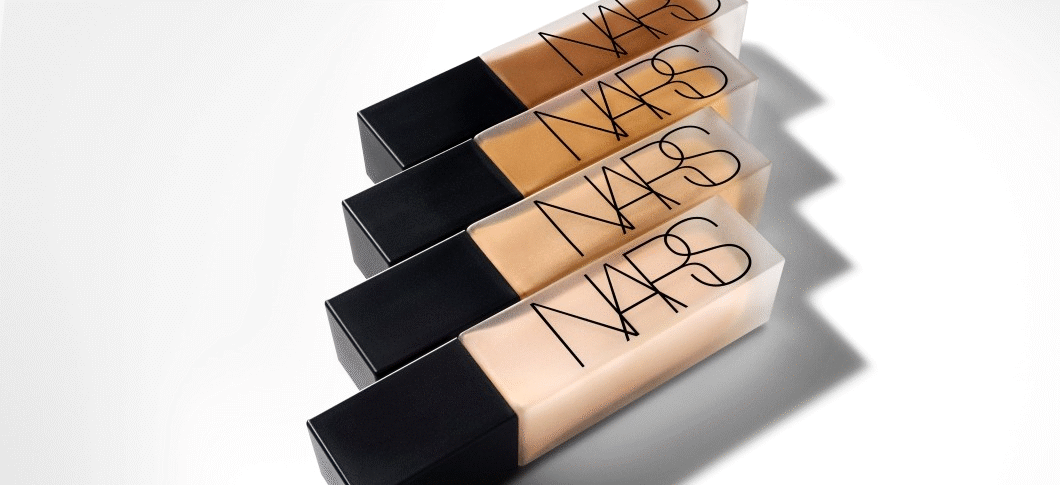 Her ses et billede med fire foundation-produkter fra NARS placeret diagonalt mod en lys baggrund. På produkterne står teksten “NARS”, og de vises i forskellige hudtoner med sorte låg.