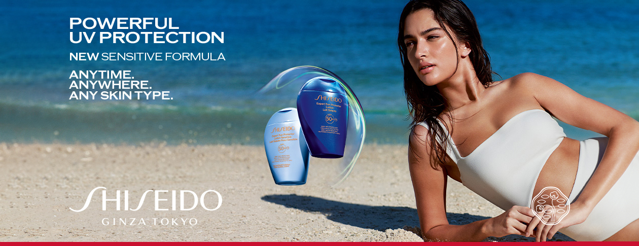 Her ses et billede med solplejeprodukter fra Shiseido placeret på en strand ved havet. På billedet står teksten “POWERFUL UV PROTECTION”, “NEW SENSITIVE FORMULA” samt “ANYTIME. ANYWHERE. ANY SKIN TYPE.” Til højre ses en person i hvid badetop, og nederst står teksten “SHISEIDO GINZA TOKYO”.