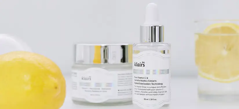 Her ses to forskellige Klairs produkter, som står i midten af vandglas og citroner. Baggrunden er lys. 