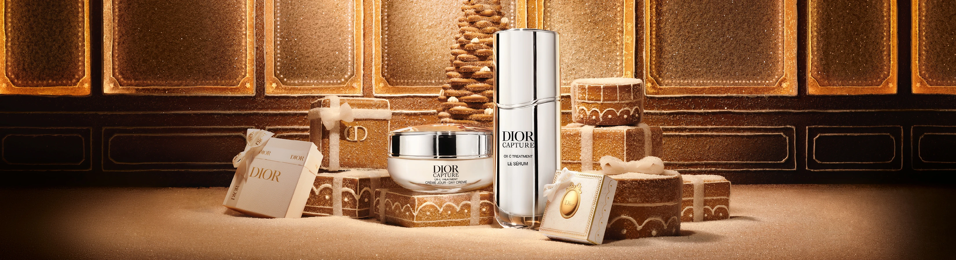 Dior Capture hudplejeprodukter, en creme og et serum, omgivet af festlige gaveæsker og et juletræ i honningkage-stil.