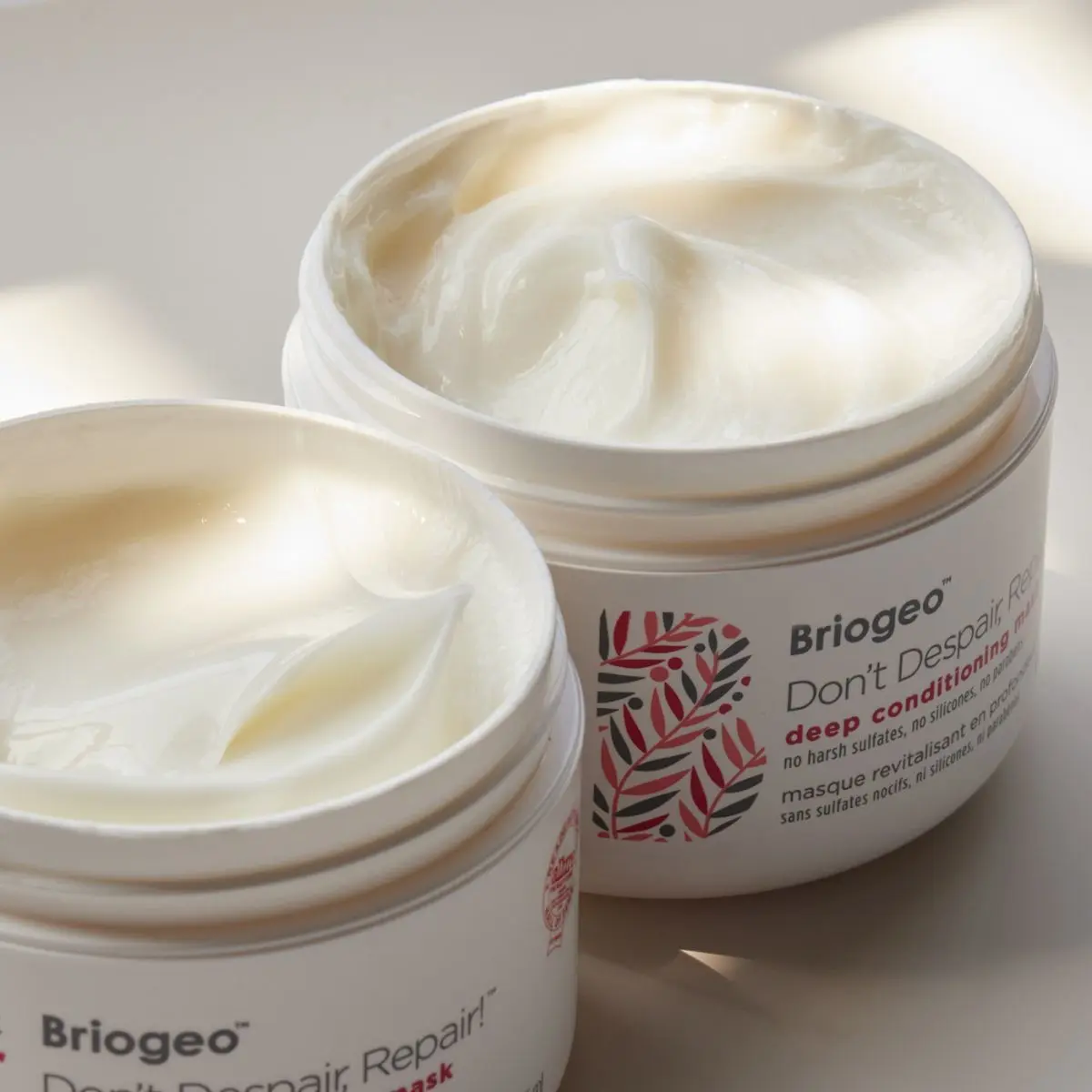 To åbne hvide krukker med Briogeo Don't Despair, Repair! dybdevirkende hårmaske, med cremehvidt produkt.