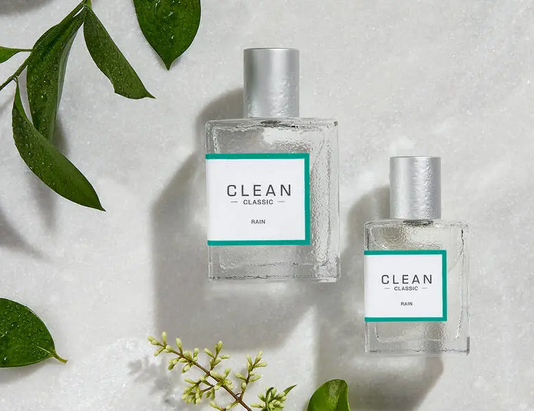 Her ses to Clean parfumer i forskellige størrelser på en hvid baggrund med nogle planter. 