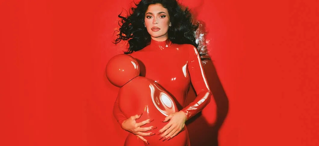 Her ses et billede af Kylie Jenner i rødt tøj, der holder en stor "Cosmic Intense" parfume foran sig. Baggrunden er også rød.