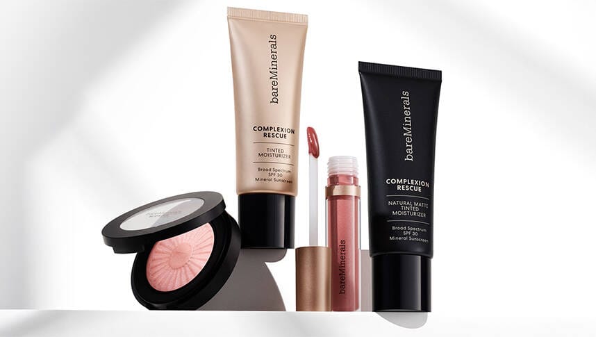 Her ses fire forskellige bareMinerals produkter på en hvid baggrund i sollys; en blish, to tinted moisturizers og en lipgloss.