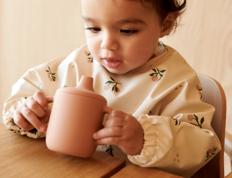 Her ses et lille barn, som har en sippy cup i hænderne. 