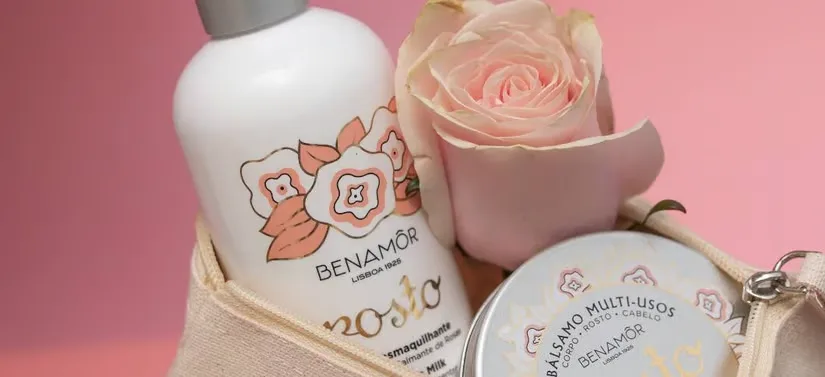 Her ses en lyserød baggrund med en beige taske, som har to produkter og en lyserød rose i sig.