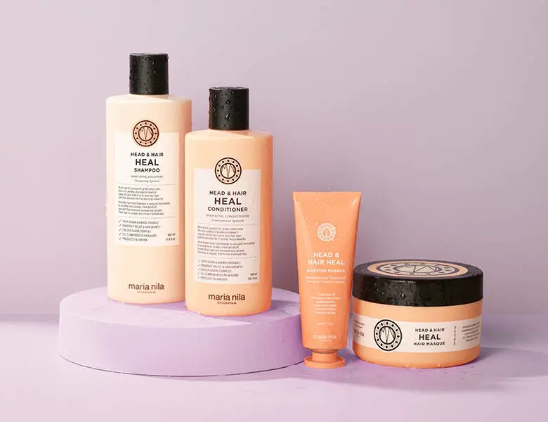 Her ses en lyselilla baggrund med fire orange Maria Nila produkter.