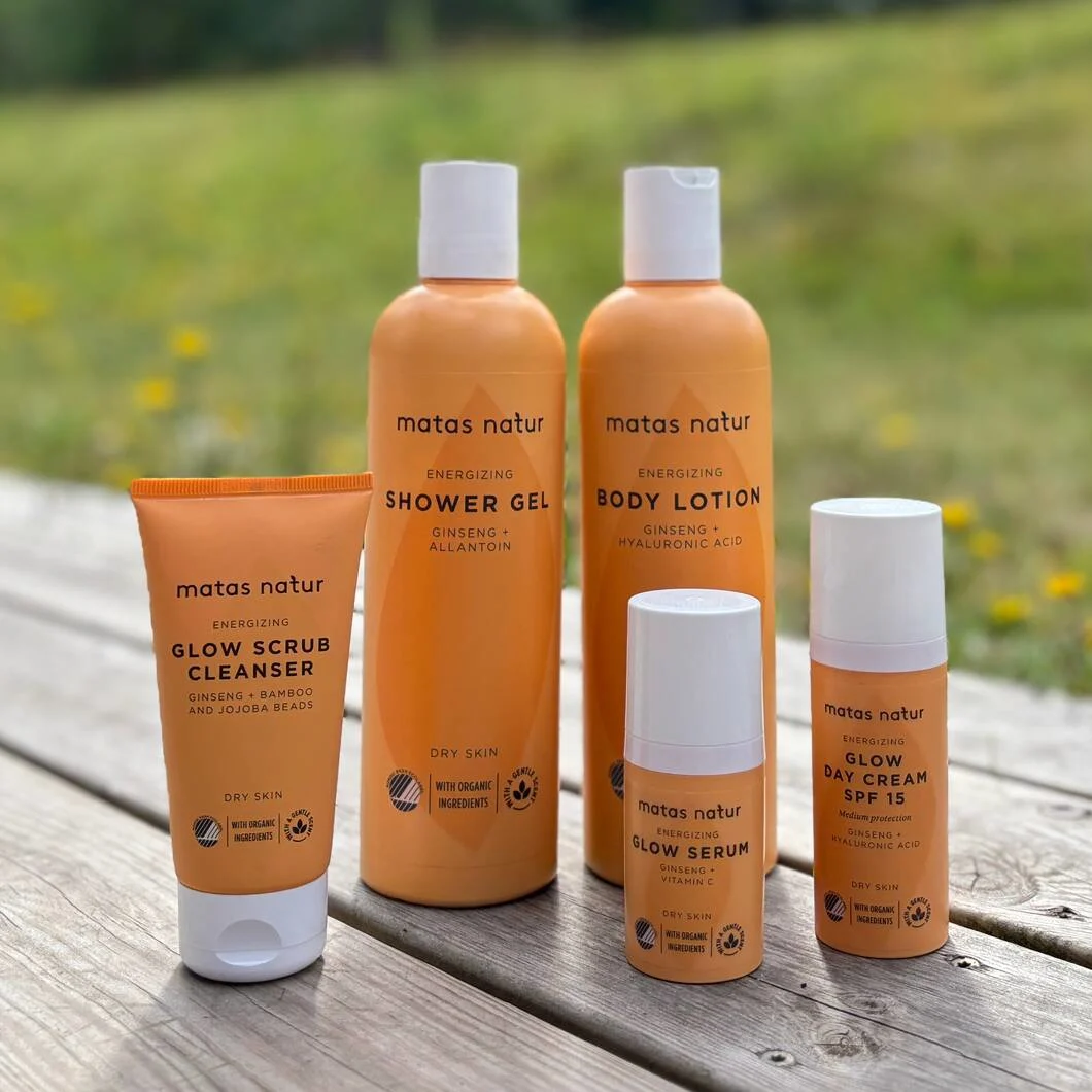 Her ses fem orange og hvide Matas Natur Energizing produkter. De står på en træterrasse med en græsplæne i baggrunden.