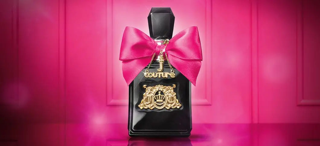 Her ses en sort Juicy Couture parfume med en pink sløjfe foran en pink baggrund