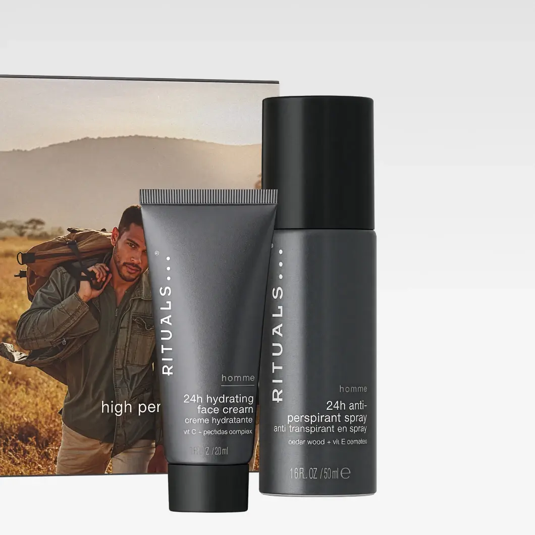 Rituals Homme med 24h Hydrating Face Cream, crème hydratante, vit C + peptides complex, 20 ml, og 24h Anti-Perspirant Spray, cedar wood + vit E complex, 50 ml. Bak produktene vises en emballasje med en person som bærer en ryggsekk utendørs og delvis synlig tekst «high per».