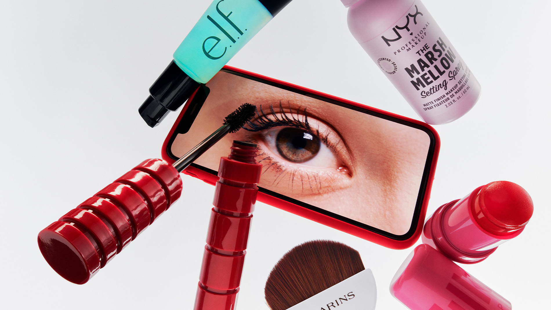 Sminkprodukter runt en mobiltelefon som visar ett öga med mascara.