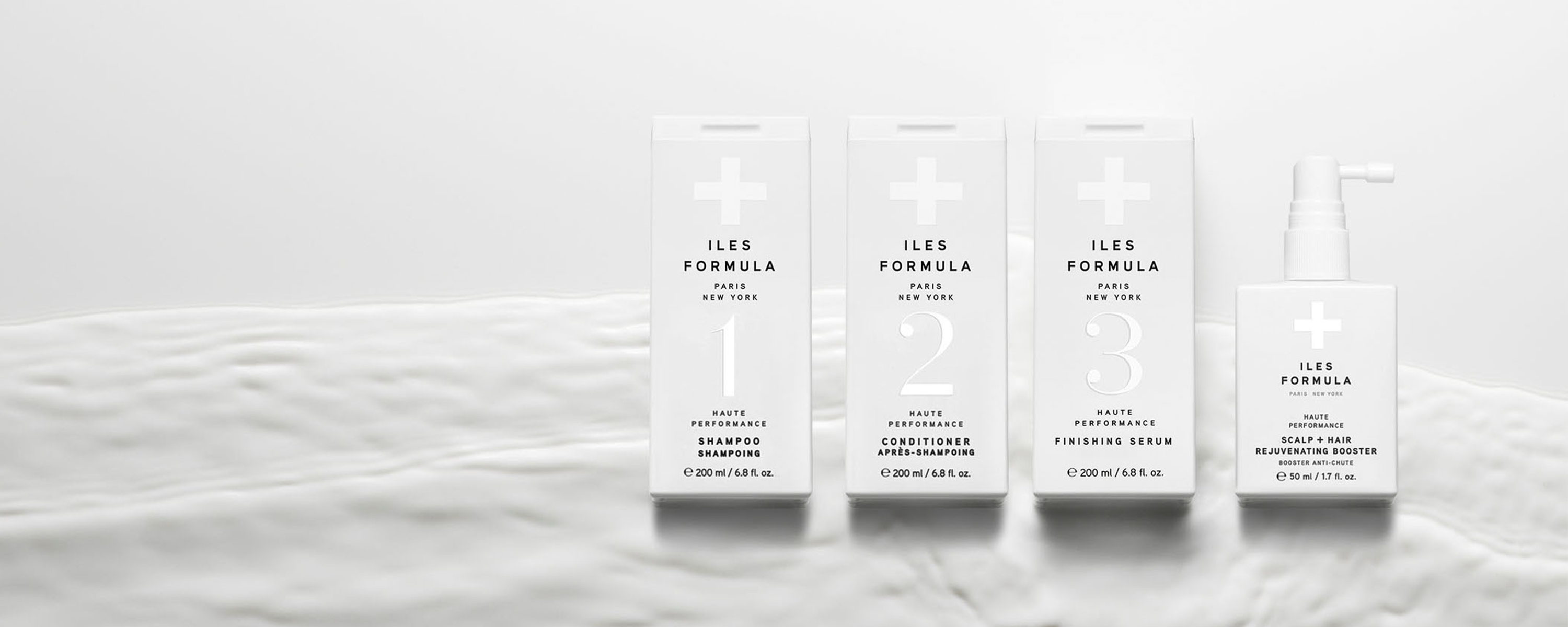 Fire hårpleieprodukter fra Iles Formula. Produktene er plassert på en hvit flate og har en minimalistisk, hvit emballasje.
