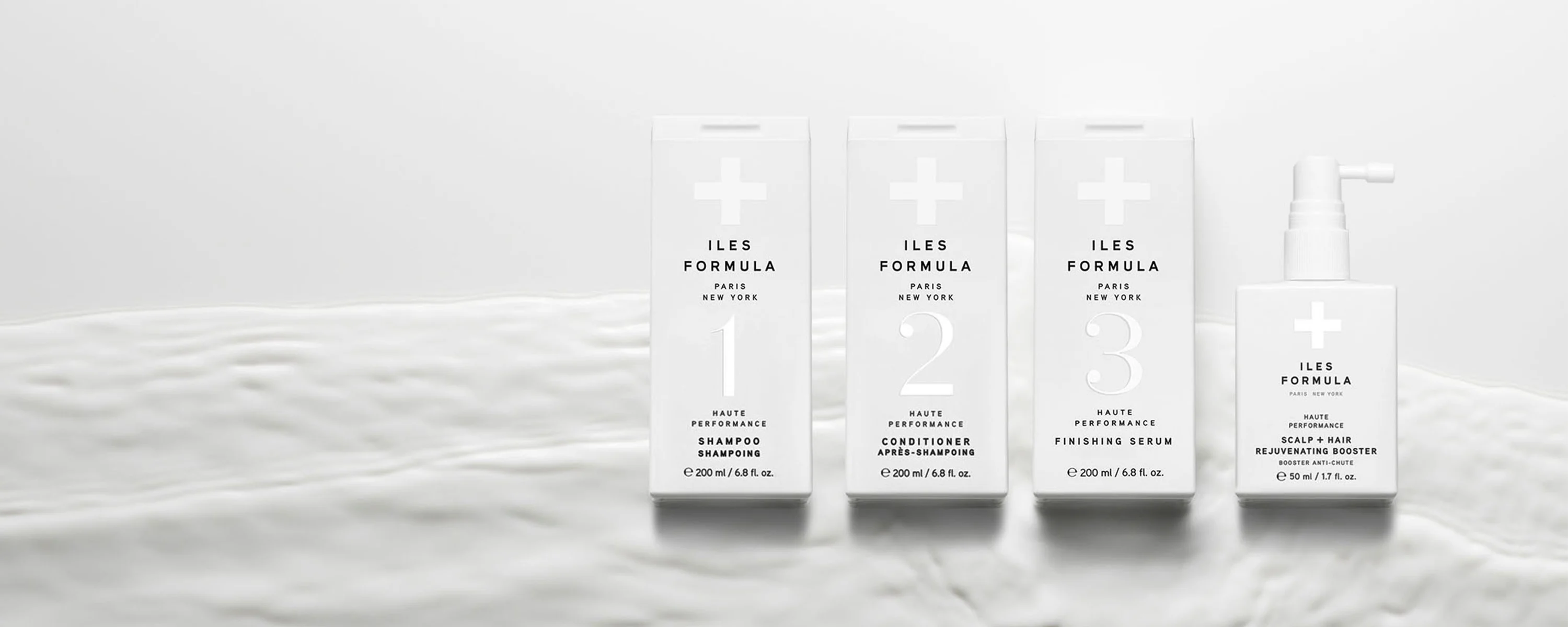 Fire hårpleieprodukter fra Iles Formula. Produktene er plassert på en hvit flate og har en minimalistisk, hvit emballasje.