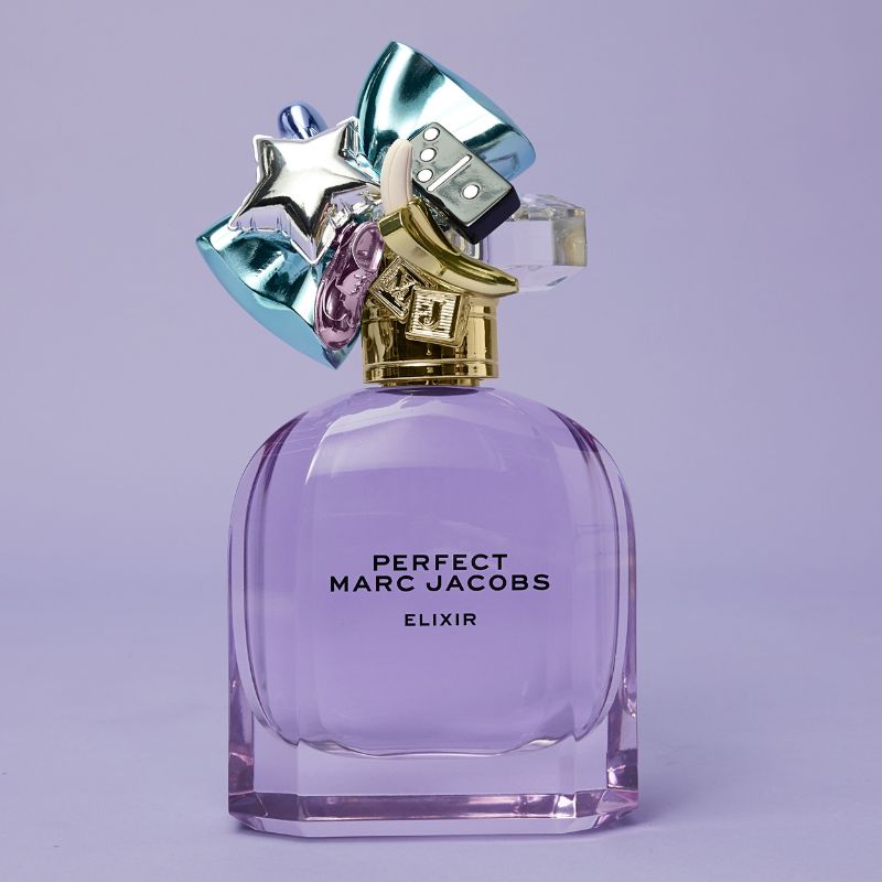 Marc Jacobsin violetti hajuvesipullo, jonka etupuolella on teksti ”Perfect Match Perfect Marc Jacobs Elixir”. Pullossa on koristeellinen korkki, jossa on erilaisia värikkäitä ja kiiltäviä muotoja, kuten tähti, banaani ja noppa. Tausta on vaalean violetti.