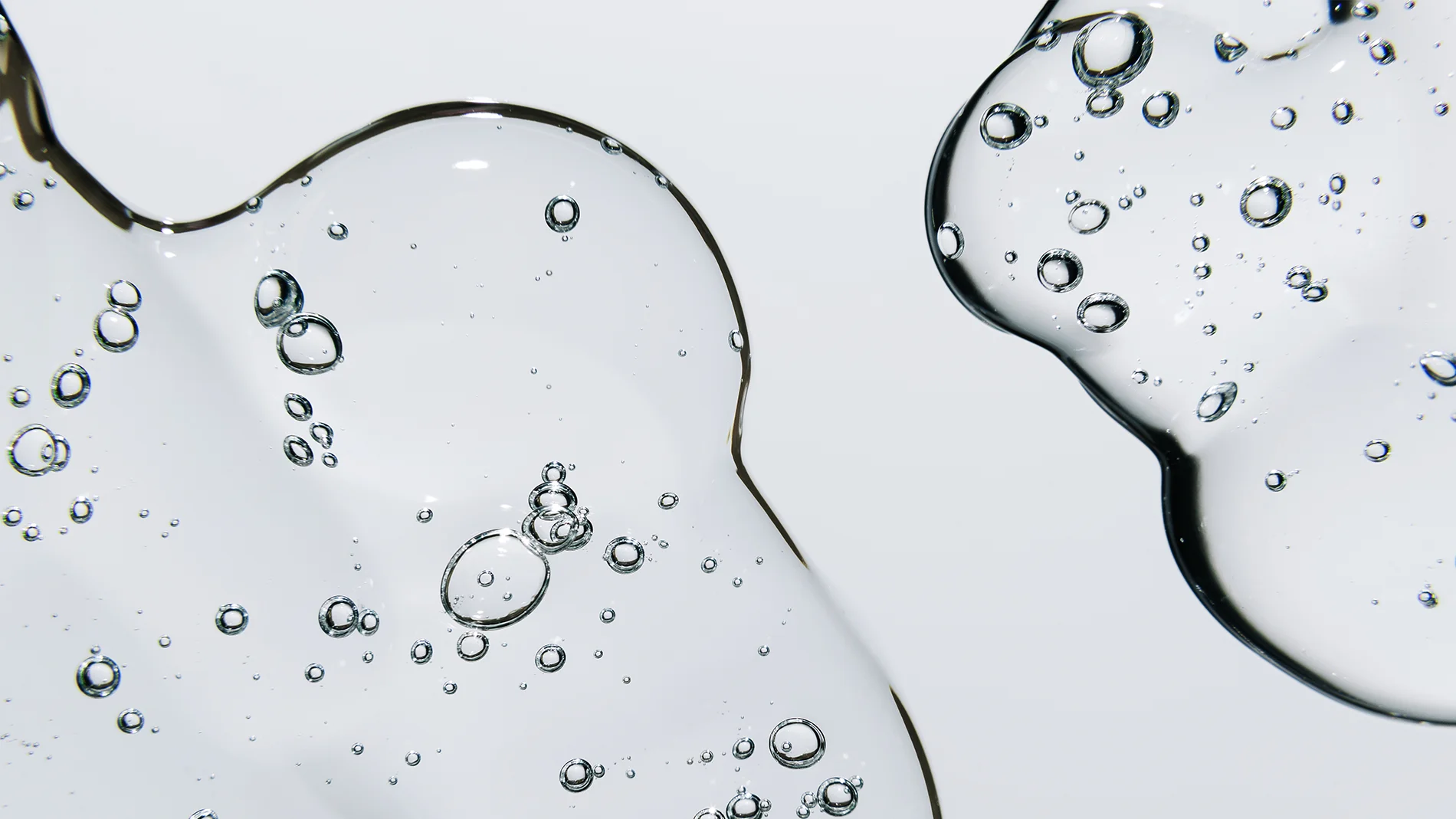 Lähikuva kirkkaasta geelimäisestä ihonhoitotekstuurista, jossa on pieniä ilmakuplia vaaleaa taustaa vasten.