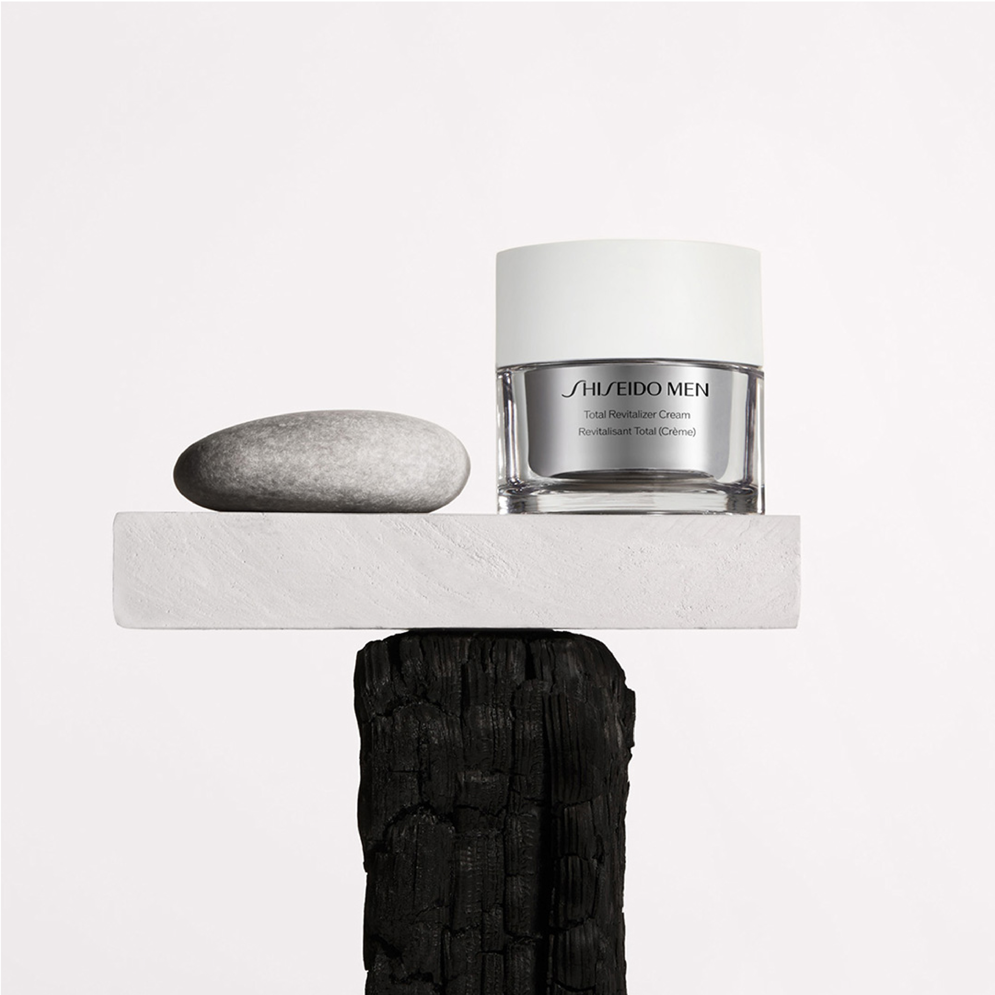 En Shiseido-kräm i en silverfärgad burk, placerad på en vit piedestal med en grå sten bredvid.