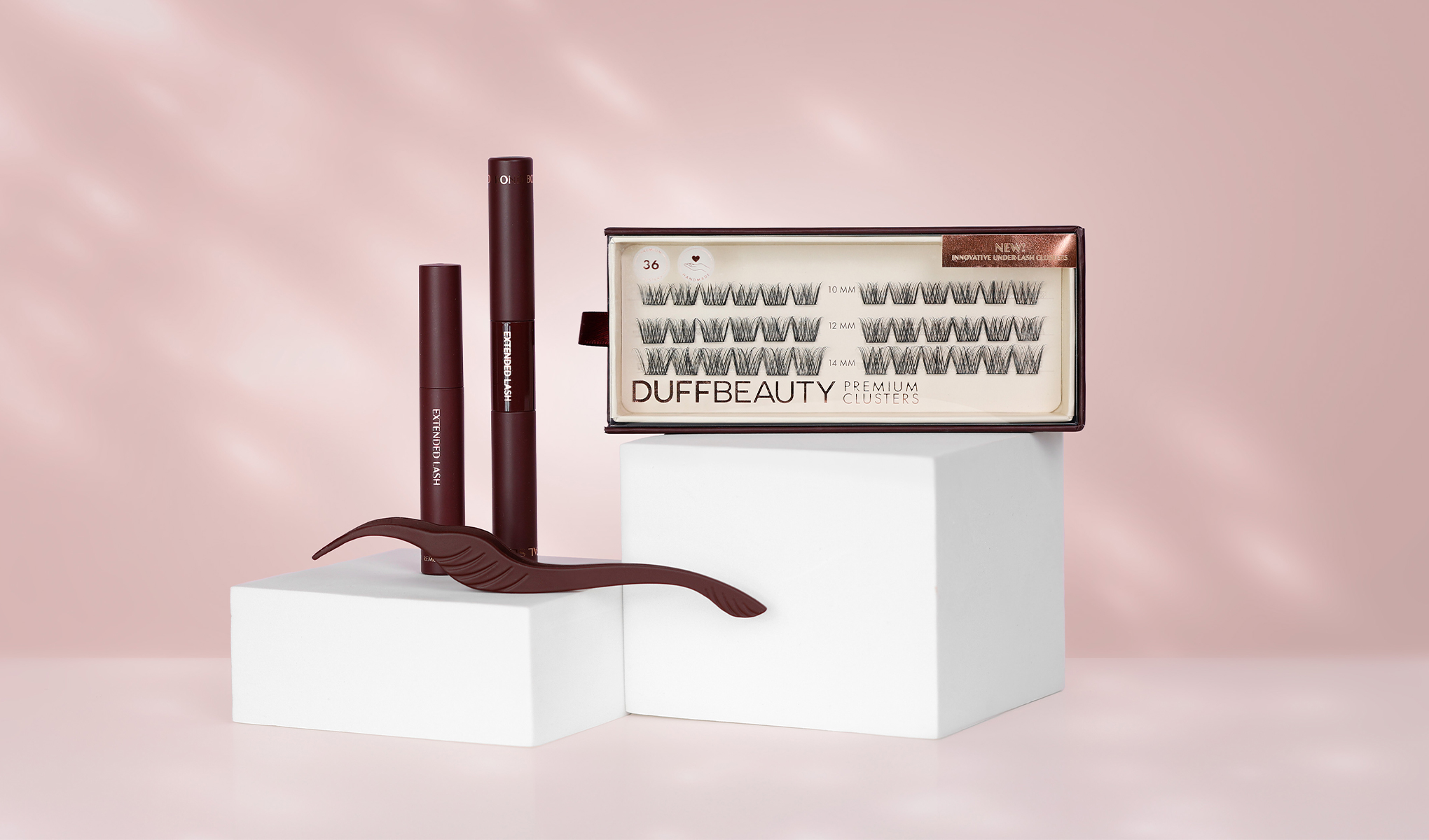 DuffBeauty-vippekluster og to vippeforlengelsesprodukter mot en rosa bakgrunn. På den hvite sokkelen er det også et brunt verktøy for vippeforlengelse.