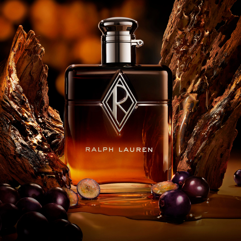 Ralph Lauren-parfymflaska omgiven av mörka vindruvor och trä i varmt ljus.