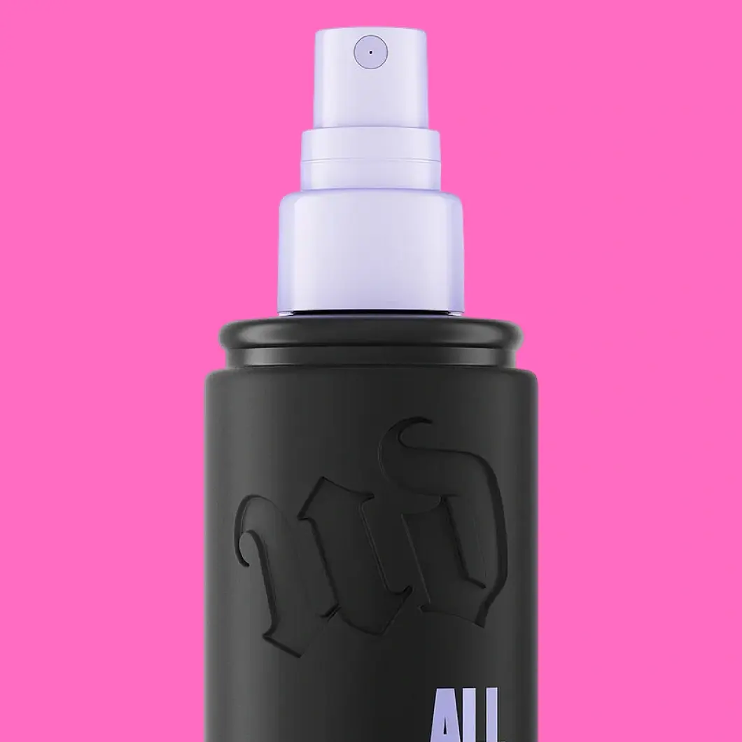 Urban Decay All Nighter setting spray i en svart flaske med lavendelfarget dyse på rosa bakgrunn.